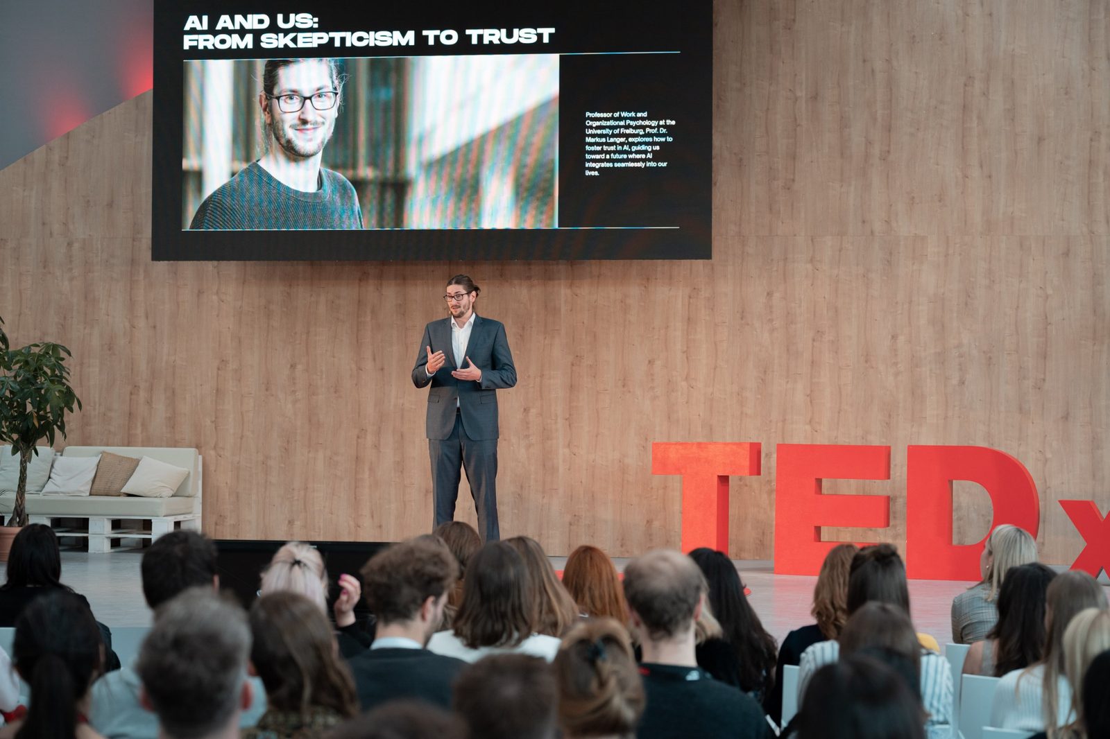 Markus Langer auf der Bühne bei TEDx Mitte in Berlin, im Hintergrund die Folie „AI and Us: From Skepticism to Trust“